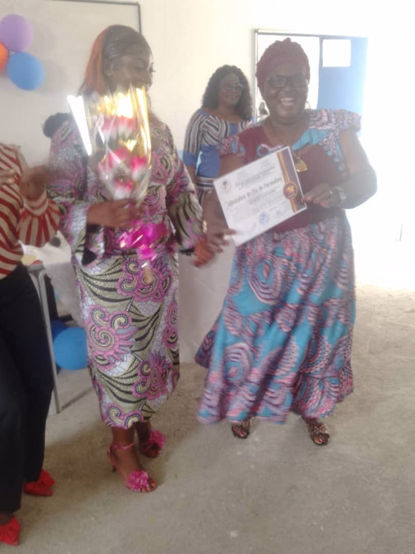 Une lauréate, bouquet à la main, et une invitée présentant son attestation de fin de formation.