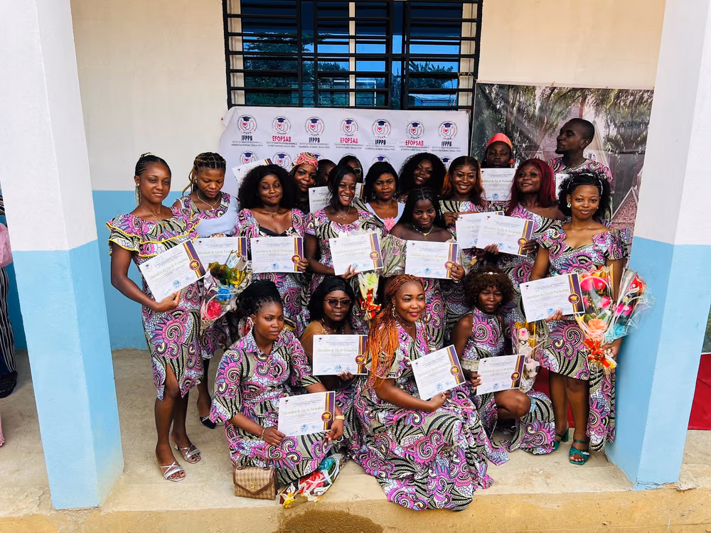Une promotion de diplômées en tenue traditionnelle assortie pose avec ses attestations de fin de formation devant la banderole de l'institut.