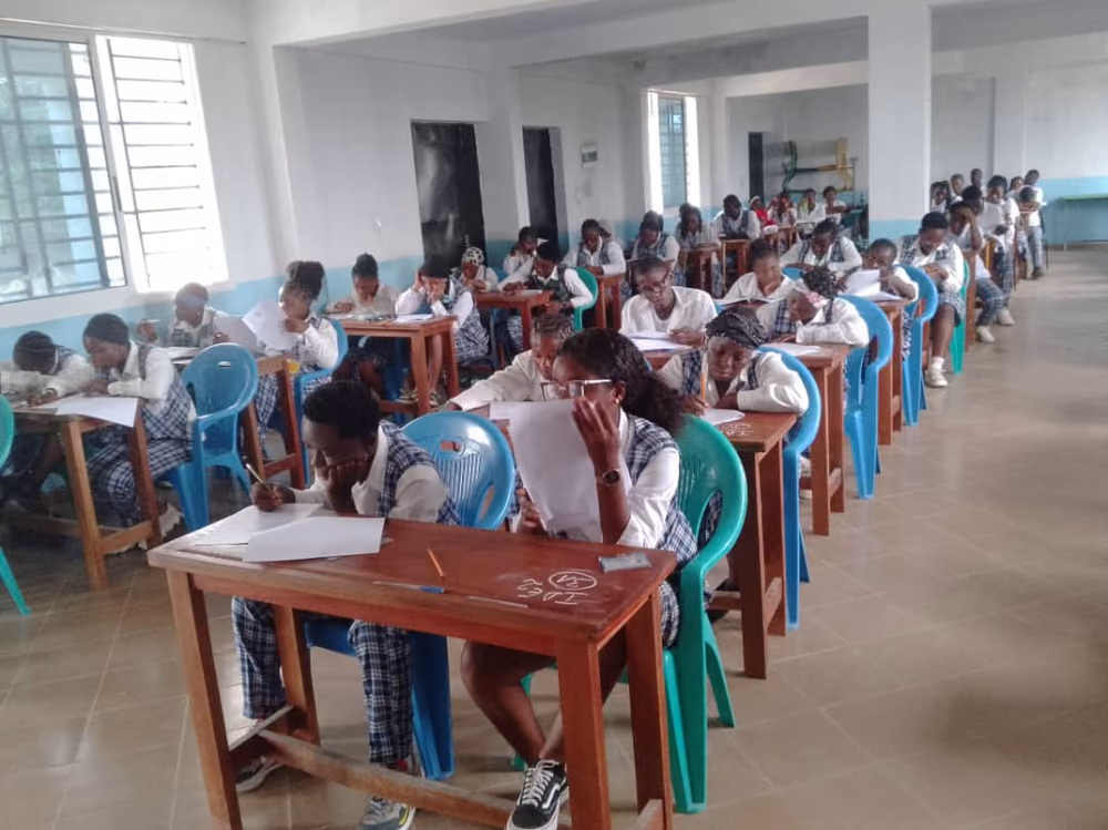 Vue en enfilade d'une salle d'examen, les apprenantes penchées sur leurs copies.
